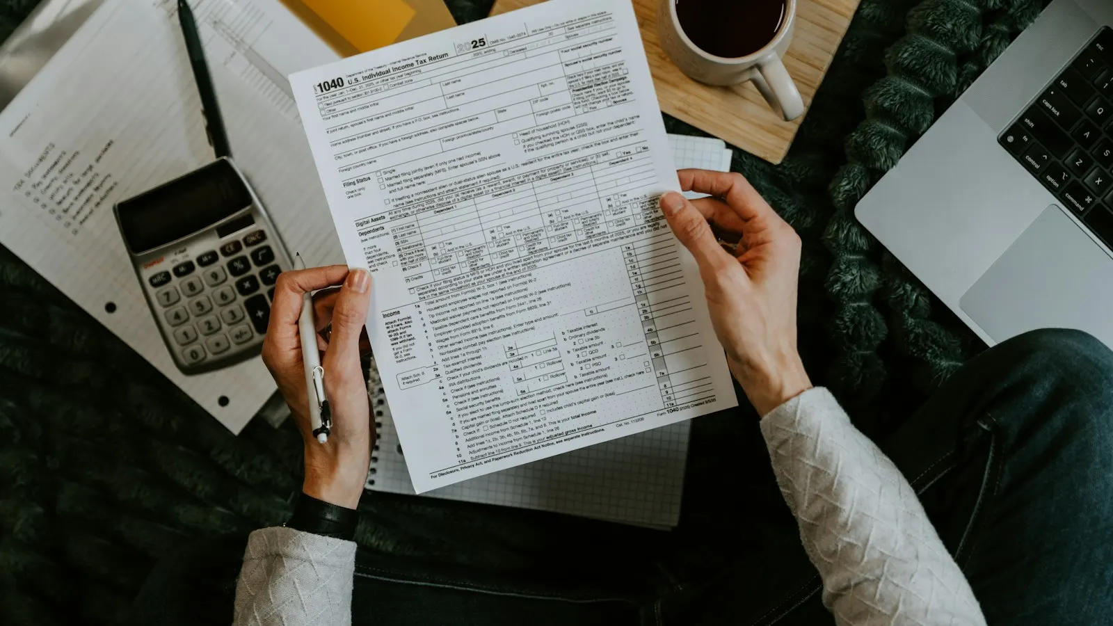 Hands reviewing a U.S. tax form beside a calculator and laptop.